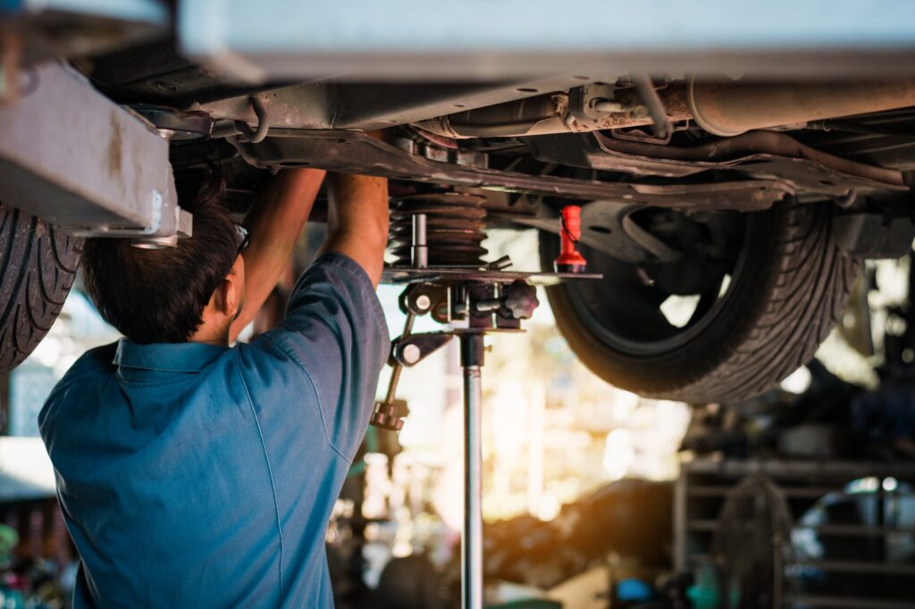 Tesla body shop mechanic in Miami performing certified collision repair underneath a vehicle.